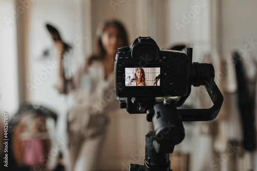 Woman posing for camera and smiling. Snaphot of black camera taking photo of charming brunette girl holding shoes photo