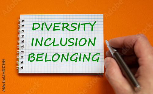 Diversity, inclusion, belonging symbol. Businessman writing words 'Diversity, inclusion, belonging' on white note, orange background. Business, diversity, inclusion, belonging concept. Copy space.