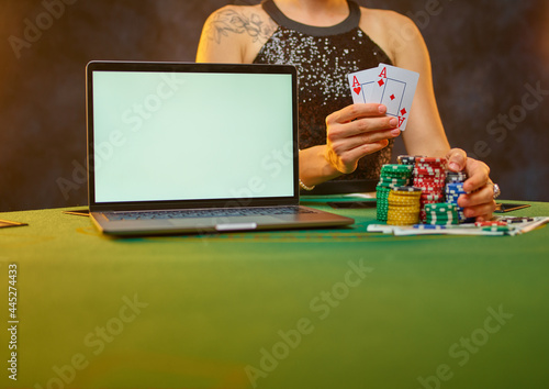 A lady in a smart dress plays poker online. She has playing cards in her hand. Colored cards lie near the laptop. Hope for a win, a good bet. Free time. Gambling business. Gambling addiction......