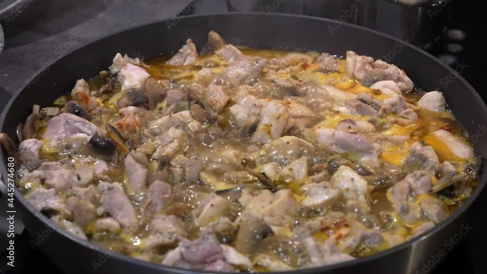 A dish of chicken, vegetables and mushrooms boils in a frying pan filled with sauce. on a ceramic electric stove. Cooking delicious and healthy food at home. slow motion A dish of chicken, vegetables and mushrooms boils in a frying pan filled with sauce. on a ceramic electric stove. Cooking delicious and healthy food at home. slow motion