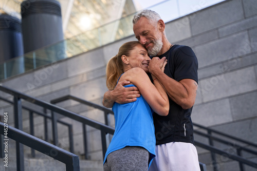 Affectionate middle aged couple, man and woman in sportswear embracing each other while standing together outdoors