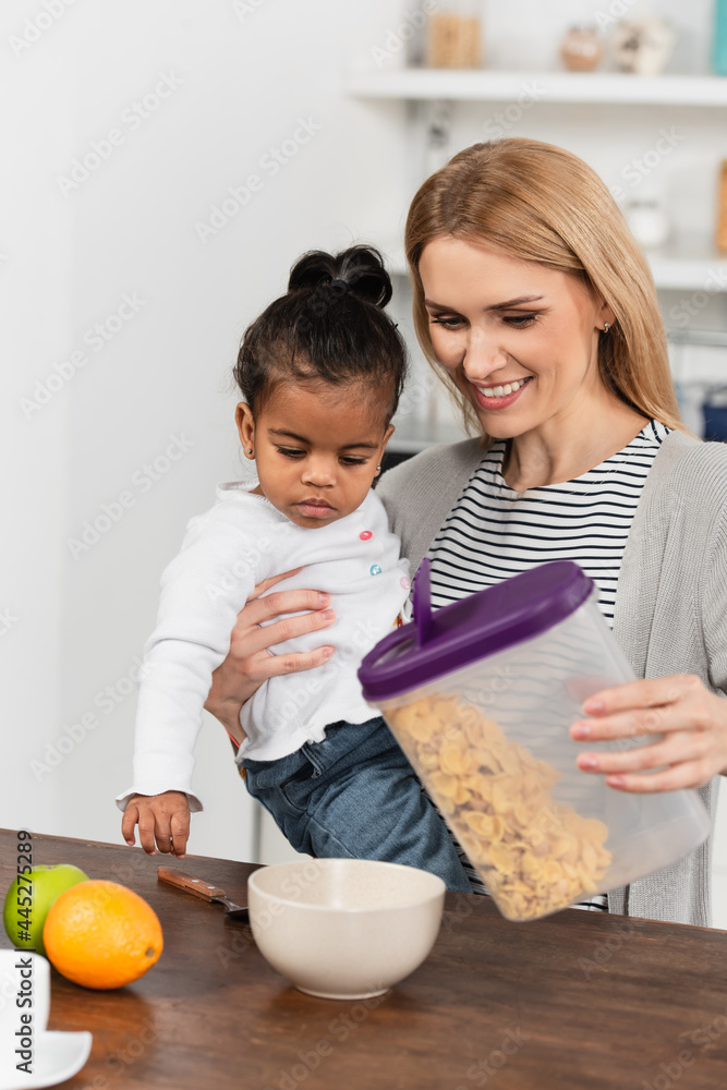 happy mother holding adopted african american kid and container with corn flakes happy mother holding adopted african american kid and container with corn flakes