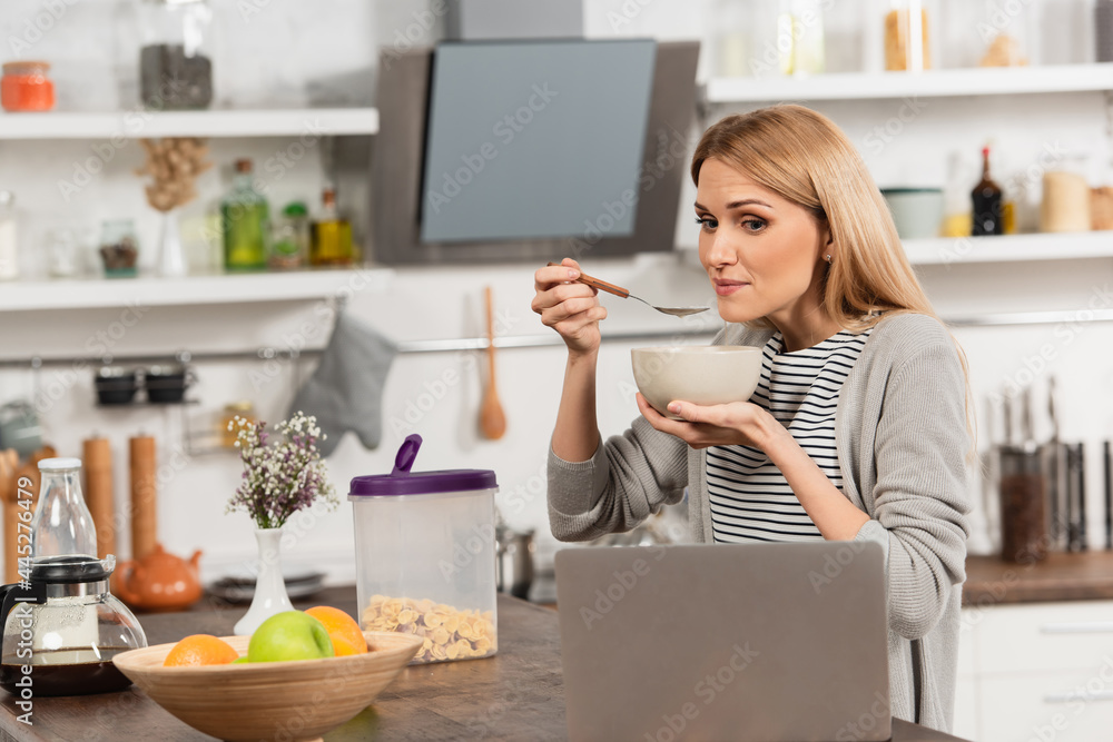 blonde woman having breakfast and watching movie on laptop in kitchen blonde woman having breakfast and watching movie on laptop in kitchen