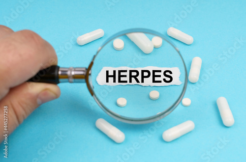 A man looks through a magnifying glass at pills and a leaf with the inscription - HERPES