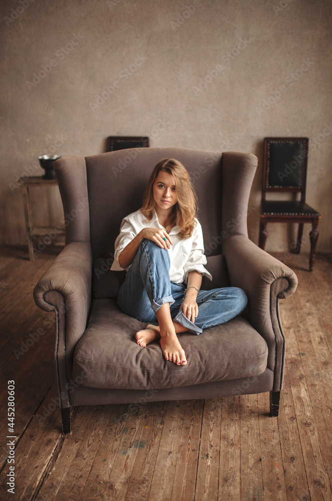 Obraz premium Attractive blond hair female sitting in armchair and looking at the camera