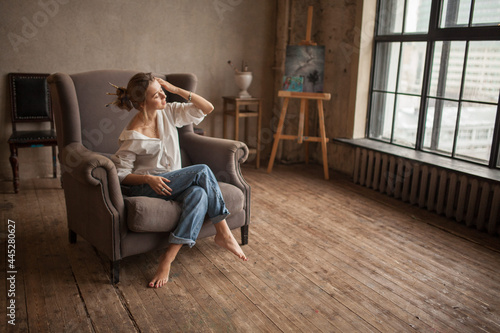 Attractive blond hair female sitting in  armchair and looking at the window