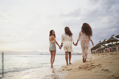 Three sisters dressed in white walking on beach. One looking at camera