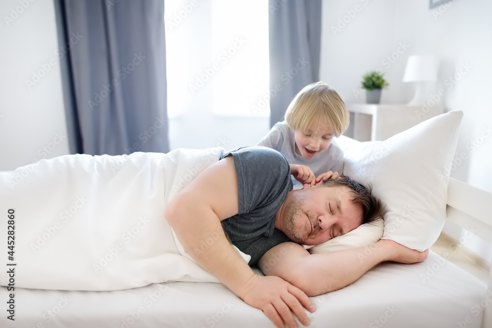 Little child awake, early in the morning he wakes up his sleeping father in bed at home. The tired dad hears nothing, sleeps and does not wake up. Parenthood. Raising children. Little child awake, early in the morning he wakes up his sleeping father in bed at home. The tired dad hears nothing, sleeps and does not wake up. Parenthood. Raising children.