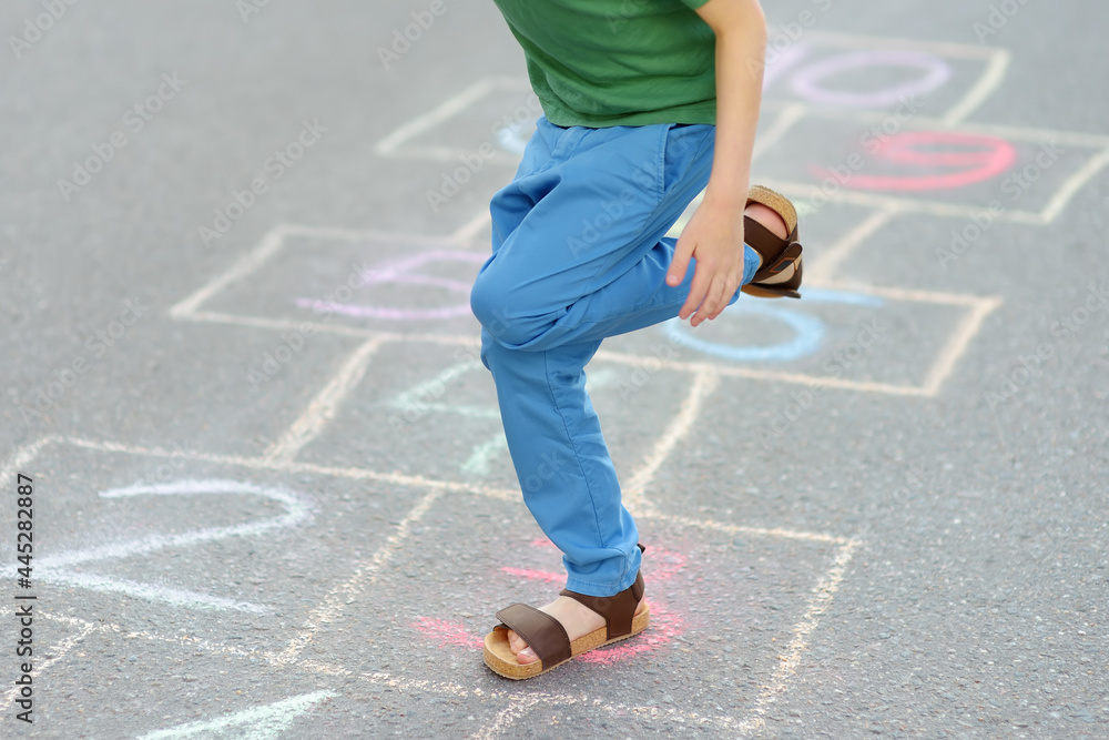 Little boy's legs and hopscotch drawn on asphalt. Child playing hopscotch game on playground on spring day.