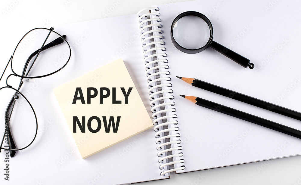 Text APPLY NOW on the sticker with keyboard , pencils and office tools Text APPLY NOW on the sticker with keyboard , pencils and office tools