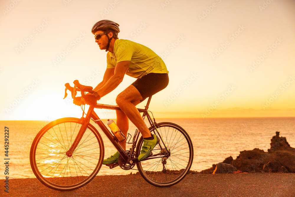 Cyclist man athlete training for triathlon riding road bike at sunset on ocean coast landscape. Triathlete exercise workout outdoor during summer.