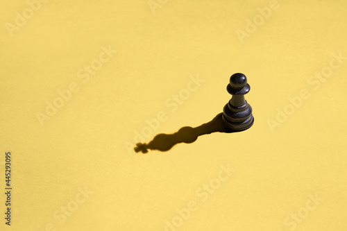Black pawn with kings shadow on yellow background photo