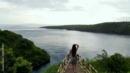 Female traveler walking to edge of wooden platform overlooking bay at sunset photo
