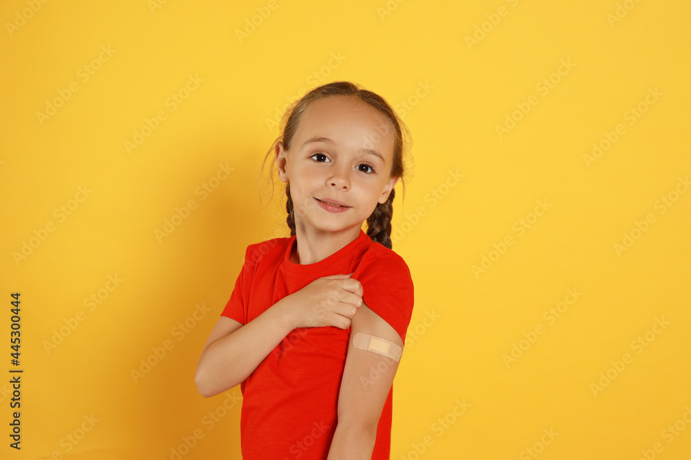 Vaccinated little girl showing medical plaster on her arm against yellow background Vaccinated little girl showing medical plaster on her arm against yellow background