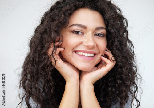 cheerful positive young mixed race female with brunette curly hair, smiling broadly, showing her white teeth at camera