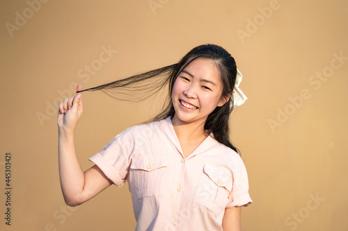 Cute Shy Asian Woman smile and play her hair in orange brown background at outdoor field in sunlight environment. photo