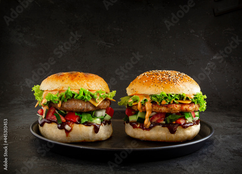Fresh tasty burgers with chicken and pork on dark background. Fat unhealthy street food.