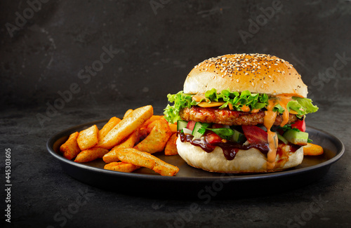 Fresh tasty burger with chicken, salad, cheesee, sauces and with french fries on dark background. Fat unhealthy street food. photo