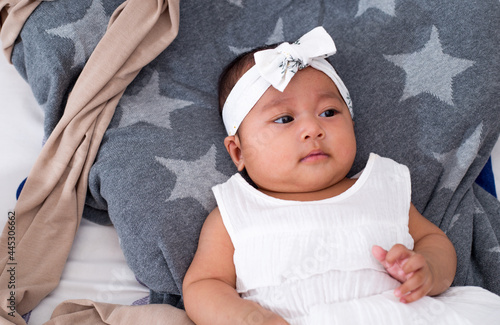 Top view portrait of a healthy baby girl dressing in white laying on bed looking up. 