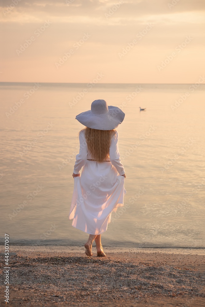 A girl in a hat at sunset on the beach