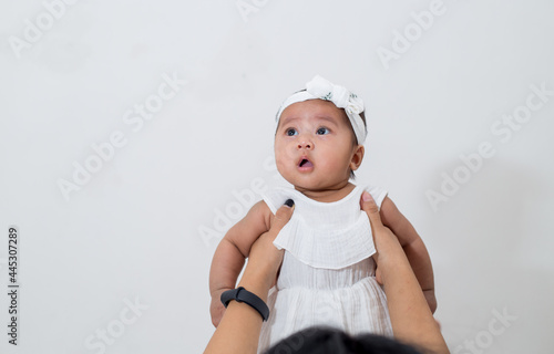 Family lifestyle portrait of mother holding her 4 months old baby girl in white dress, playing together. 