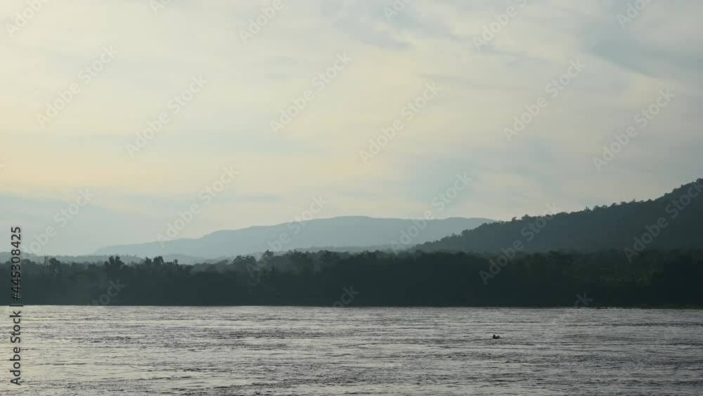 Mekong River flowing as a boat seen in the middle drifting towards the right off the frame, lovely hazy horizon of forest and hills. Mekong River flowing as a boat seen in the middle drifting towards the right off the frame, lovely hazy horizon of forest and hills.