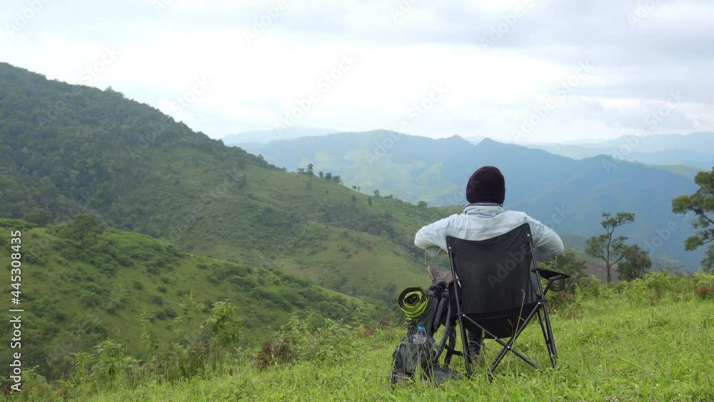 Asian man sitting on outdoor chair looking to beautiful nature of the mountain and green meadow. Handsome male relax and enjoy outdoor activity active lifestyle hiking and camping in summer vacation. Asian man sitting on outdoor chair looking to beautiful nature of the mountain and green meadow. Handsome male relax and enjoy outdoor activity active lifestyle hiking and camping in summer vacation.