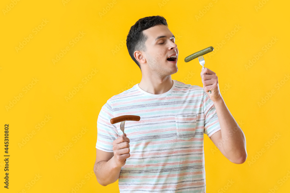 Young man eating tasty sausages on color background Young man eating tasty sausages on color background