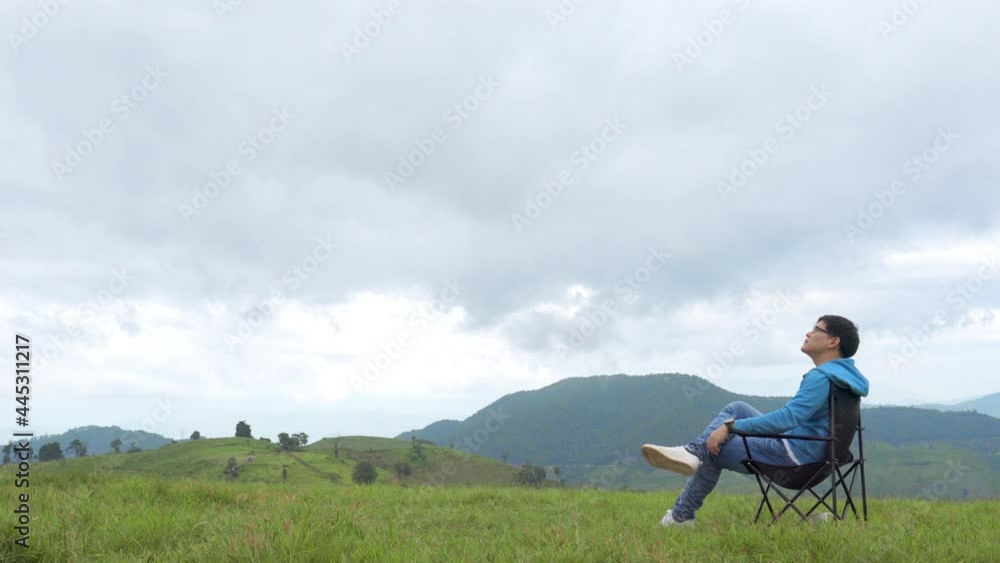 Asian man sitting on outdoor chair looking to beautiful nature of the mountain and green meadow. Handsome male relax and enjoy outdoor activity active lifestyle hiking and camping in summer vacation. Asian man sitting on outdoor chair looking to beautiful nature of the mountain and green meadow. Handsome male relax and enjoy outdoor activity active lifestyle hiking and camping in summer vacation.