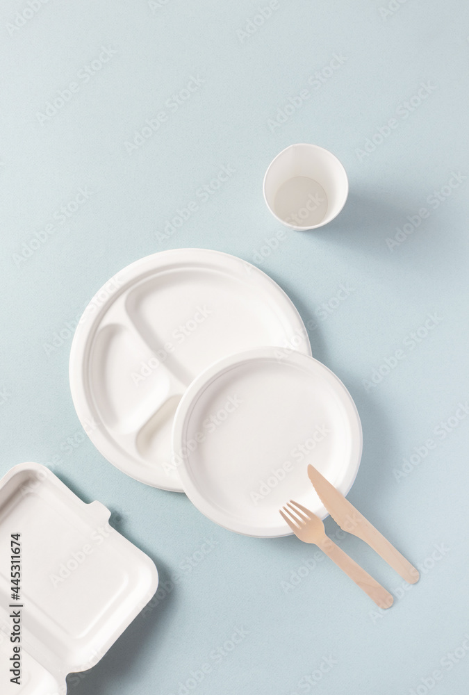 Plastic-free disposable tableware top view on blue, vertical. Paper plate, food containers, glass, wooden fork, knife. Compostable or biodegradable dinnerware non-plastic alternatives flat lay concept Plastic-free disposable tableware top view on blue, vertical. Paper plate, food containers, glass, wooden fork, knife. Compostable or biodegradable dinnerware non-plastic alternatives flat lay concept