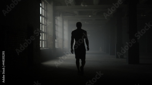 Man silhouette walking in dark corridor. Athlete taking break after workout