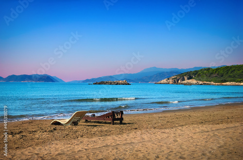 Deserted beach with sun beds in the absence of people, sand, clear blue water and distant islands at the background of morning sky. Beautiful nature scenery in Andriake beach, Demre, Antalya, Turkey. photo