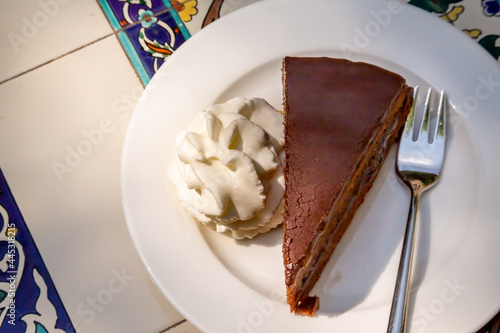 Apricot and chocolate Sacher cake with whipped cream. Sachertorte is a chocolate cake, or torte of Austrian origin, invented by Franz Sacher supposedly in 1832 for Prince Metternich in Vienna photo