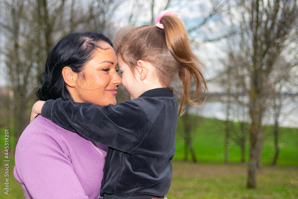 Beautiful mother and daughter play hugs in a spring park nature in profile looking at each other. Beautiful mother and daughter play hugs in a spring park nature in profile looking at each other.