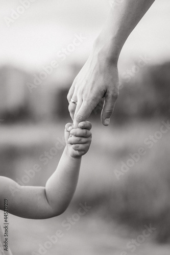 The child holds his mother's hand tightly. Black and white photo of the child with his mother. Close-up of the child's and parent's hands. A place for a text about childhood
