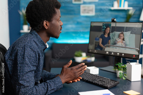 Fotografija Black man talking with his family in hospital ward, using intenet online teleconference video call to connect with loved ones