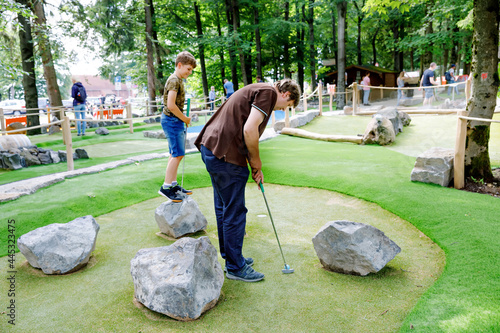 School kid boy playing mini golf with father. Happy child and dad, young man having fun with outdoor activity. Summer sport for children and adults, outdoors. Family vacations or resort. photo