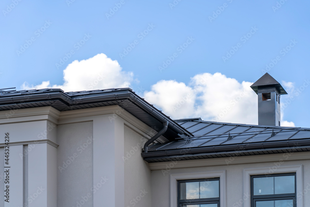 view of house with gray fold roof and plums and filing of roof overhangs with soffits and brick stone pipe covered with metal sheets and black smoke box