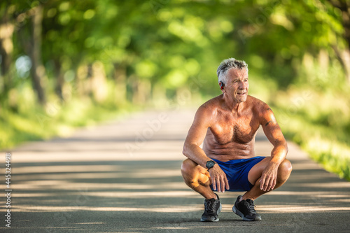 Obraz na plátne Muscular and fit older man squats as he rests after doing sport outdoors in the
