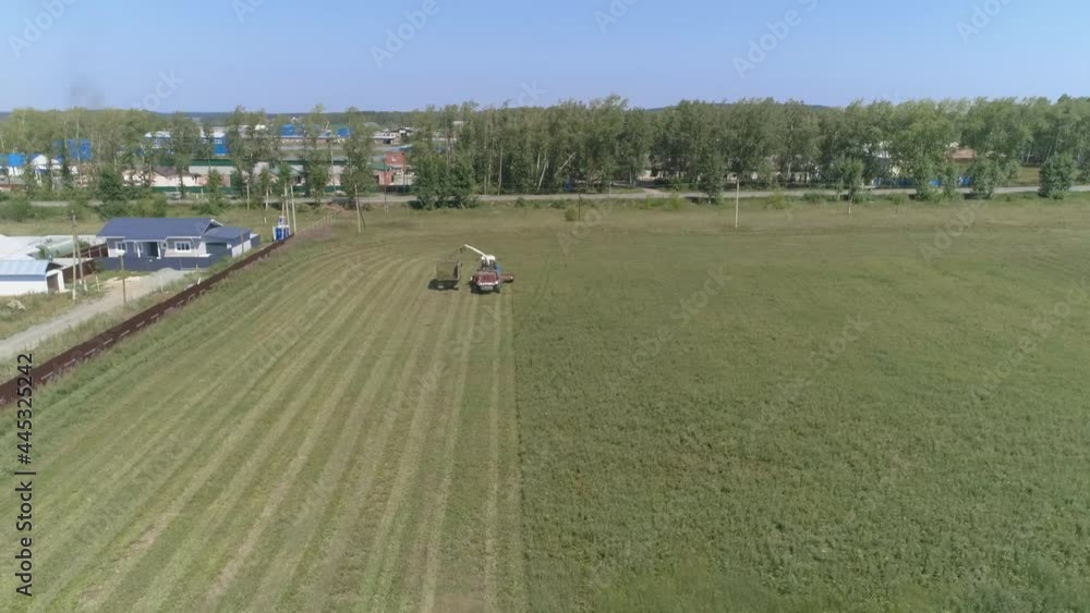 Aerial view of Combine harvesting on grass field. The harvester putting the haylage on a truck. Near the village, houses, forest, road with cars and industrial area.
Aerial view of Combine harvesting on grass field. The harvester putting the haylage on a truck. Near the village, houses, forest, road with cars and industrial area.