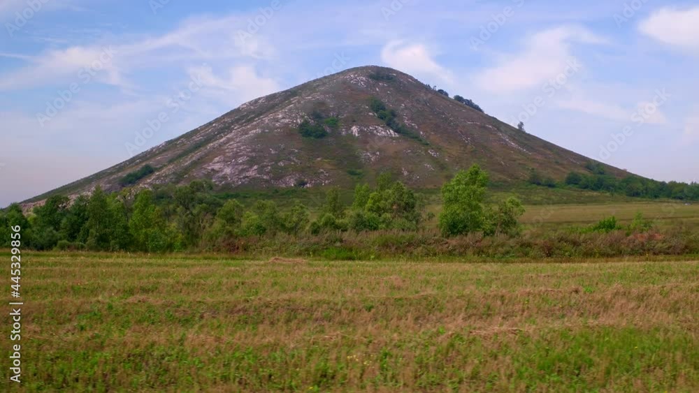 The mountain descends to a clearing overgrown with fresh green grass. Light clouds move across the blue sky. Nature, silence, a place to relax. Shooting in motion, side view. 4k footage.
