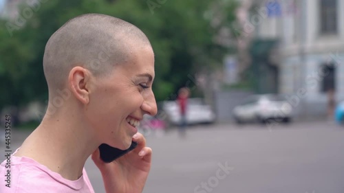 Emotional bald woman talking on mobile phone walking on the street, smiling. Slow motion 