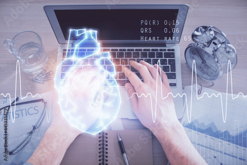 Double exposure of man's hands typing over computer keyboard and human heart hologram drawing. Top view. Medical education concept.