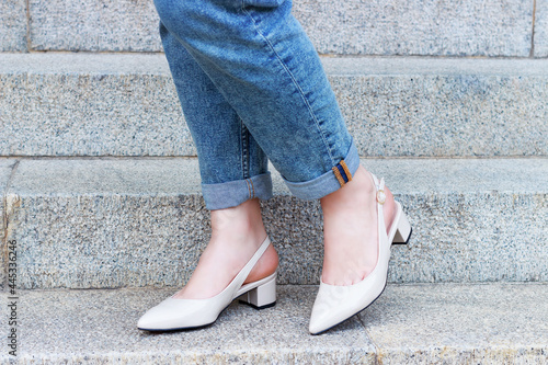 Female legs in jeans and beige shoes on the background of concrete staircase.