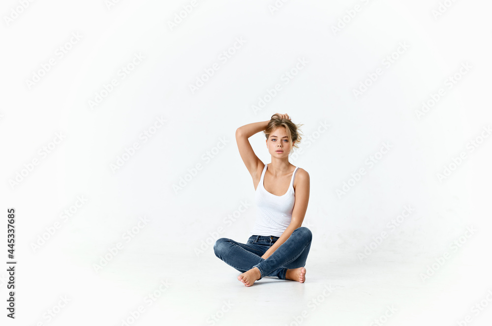 woman in white t-shirt and jeans sits on the floor holding her hair