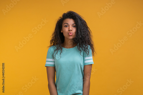 Portrait of cute attractive african american girl giving an air kiss, posing isolated over yellow background