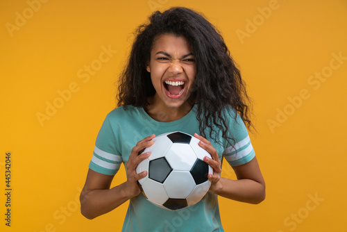 Studio image of euphoric soccer fan girl holding ball in hands looking at the camera and screaming, supporting favourite team © wpadington