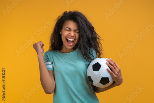 Portrait of excited soccer fan girl celebrating victory after betting at bookmaker's website, making winner's gesture clenching her fist while holding ball in hand © wpadington