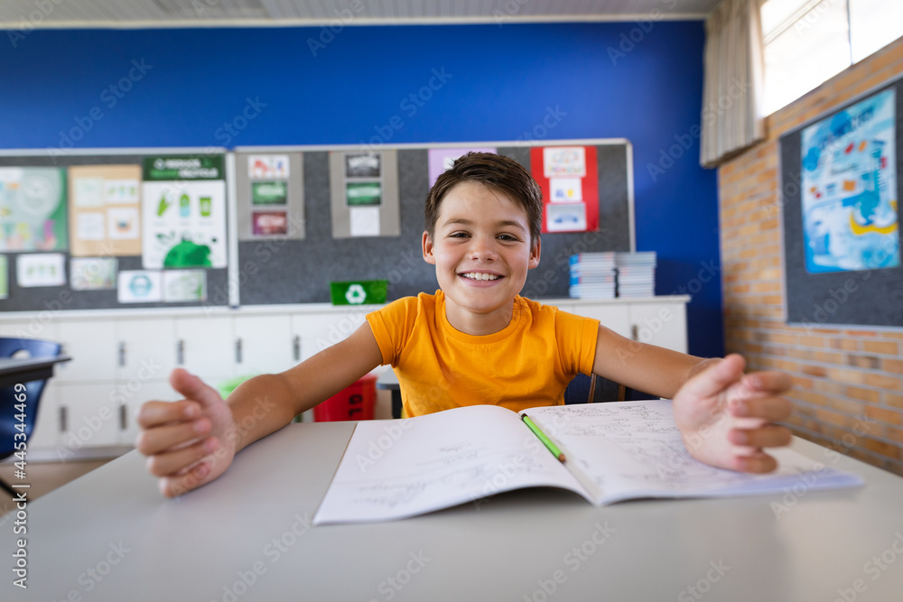 Portrait of caucasian boy smiling while sitting on his desk in the class at elementary school Portrait of caucasian boy smiling while sitting on his desk in the class at elementary school