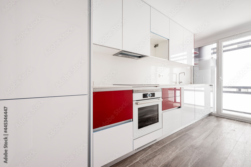 White kitchen with red touches prepared to release with an exit door to a shop terrace with appliances and a wooden stoneware floor White kitchen with red touches prepared to release with an exit door to a shop terrace with appliances and a wooden stoneware floor
